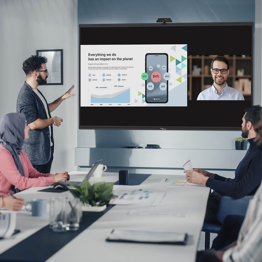 Team in hybrid meeting presents sustainability data with video conferencing and digital analytics on screen.